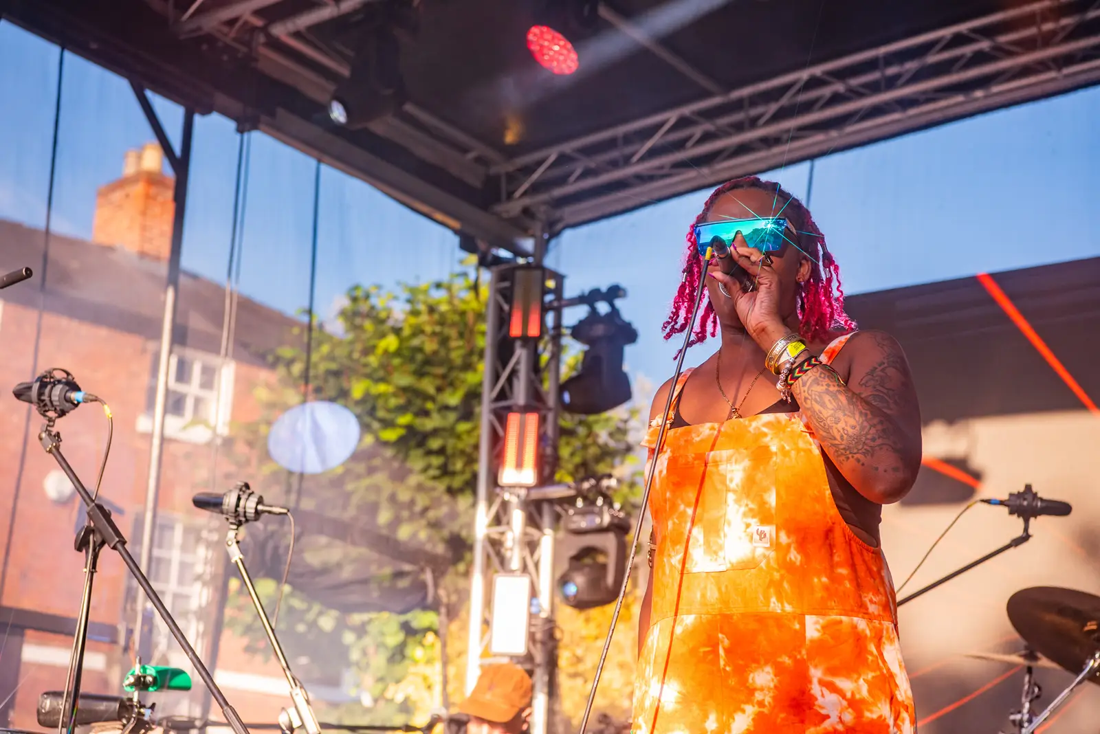 A lady, with pink hair and wearing orange dungarees, singing on a stage.